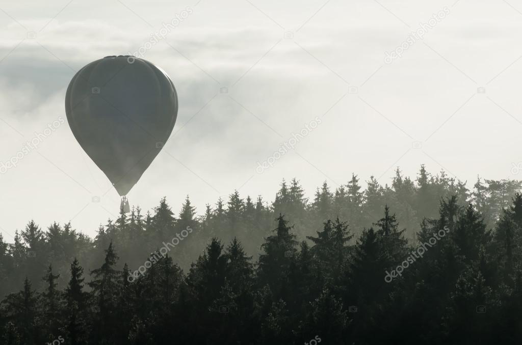 Hot air balloon above the foggy forest
