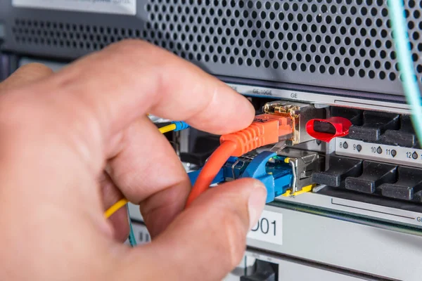 计算机技术人员将光纤电缆连接到数据交换中的手 — 图库照片