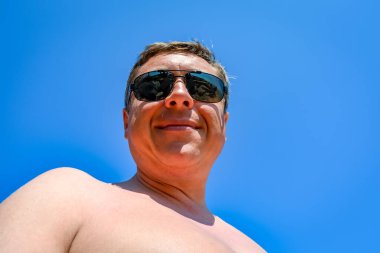 Olgun bir adam güneşli bir günde deniz kıyısında dinleniyor.