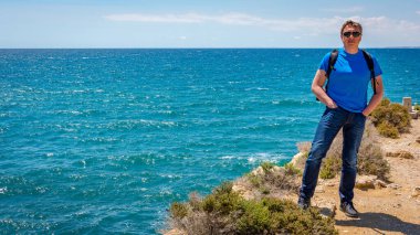 Olgun bir adam güneşli bir günde deniz kıyısında dinleniyor.