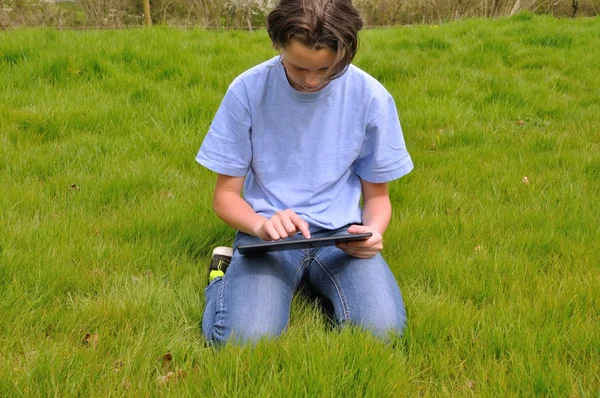 Dziewczyna siedzi na trawniku i za pomocą cyfrowego tabletu — Zdjęcie stockowe