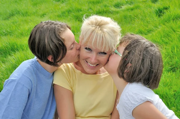 Una madre sonríe mientras recibe un beso en la mejilla de su — Foto de Stock