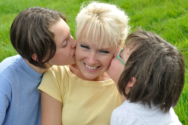 Una madre sonríe mientras recibe un beso en la mejilla de su — Foto de Stock