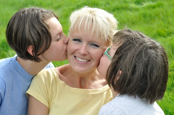 Una madre sonríe mientras recibe un beso en la mejilla de su —  Fotos de Stock
