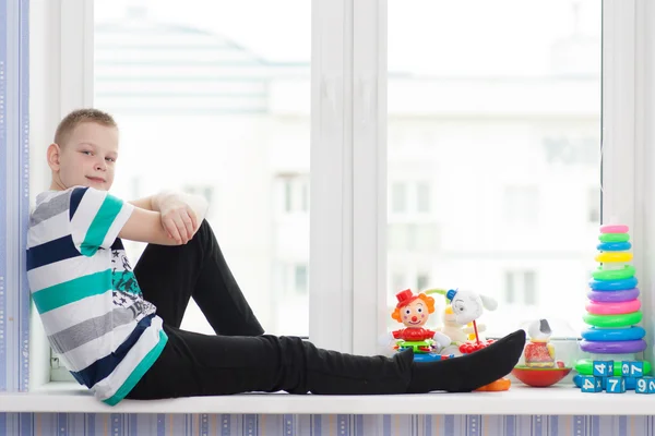 Yang chico sentado con juguetes en un alféizar de ventana — Foto de Stock