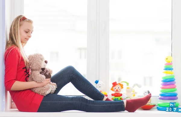 Meisje zit op een vensterbank met speelgoed — Stockfoto