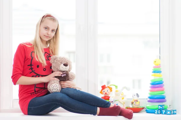 Chica se sienta en una ventana alféizar con juguetes — Foto de Stock