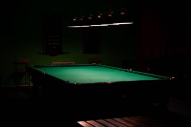 Boş bir bilardo masası, karanlık bir arka planda lamba ışığında yıkanmış..