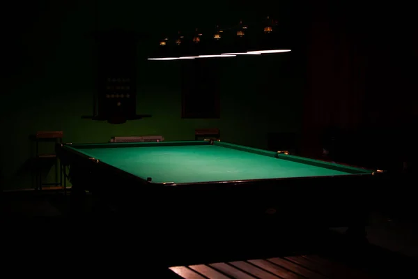 Egy üres biliárdasztal, lámpafényben fürödve, sötét háttérrel. — Stock Fotó