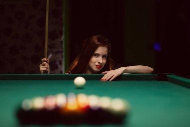 Kara bilardo kulübünde bilardo oynayan genç bir kadın.