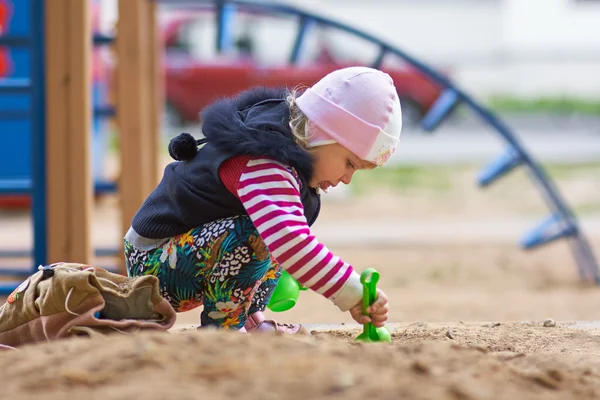 Маленькая девочка играет с песком в песочнице — стоковое фото