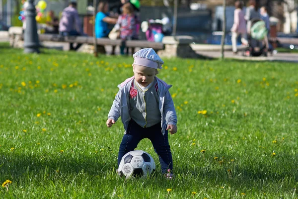 Little girl baby blond  Outdoors. Active football fan running on the green grass field with ball — Stock Photo, Image