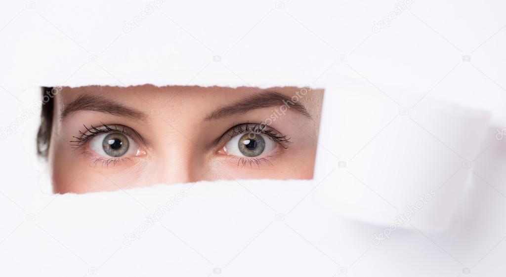 Women  eyes through a hole in a paper