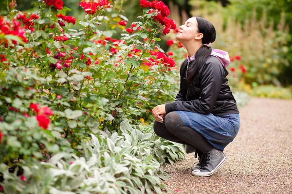 Mujer joven olfateando rosas en un jardín — Foto de Stock