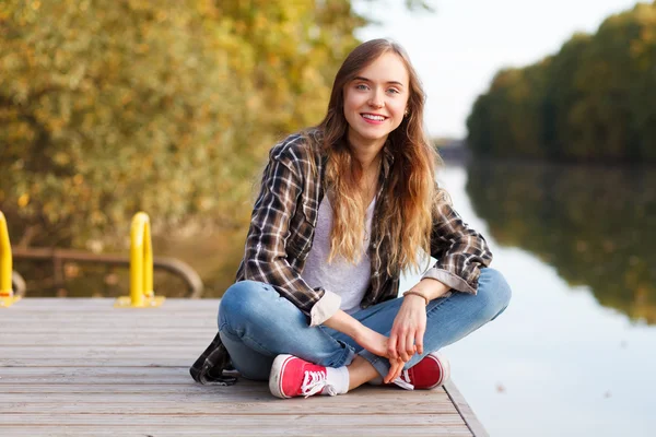 Młoda piękna dziewczyna siedzi na molo — Zdjęcie stockowe