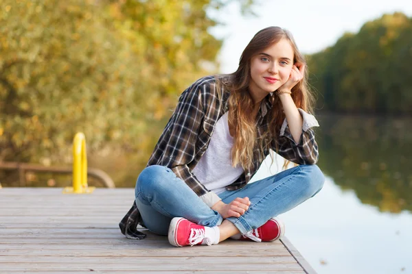 Giovane bella ragazza seduta su un molo — Foto Stock