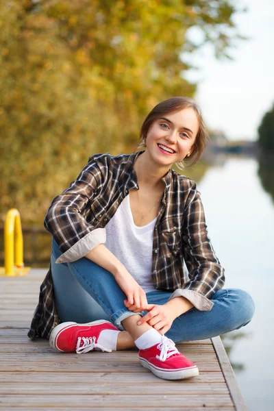 Jovem menina bonita sentada em um cais — Fotografia de Stock