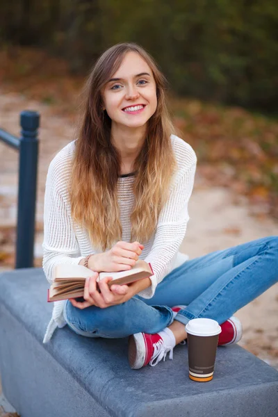 Jovem menina bonita sentada em um banco em um parque — Fotografia de Stock