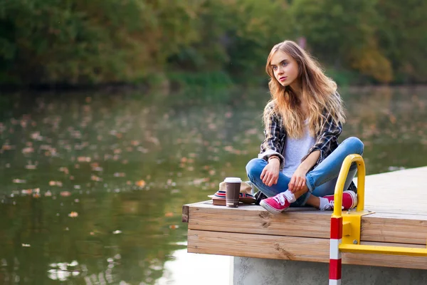 Jovem menina bonita sentada em um cais — Fotografia de Stock