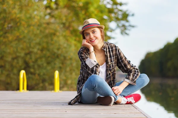 Giovane bella ragazza seduta su un molo — Foto Stock