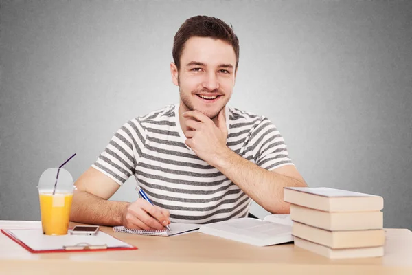 Young man sitting at the table with a pile of books — Stock Photo, Image