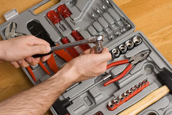 Hands holding ratchet over toolbox — Stock Photo, Image