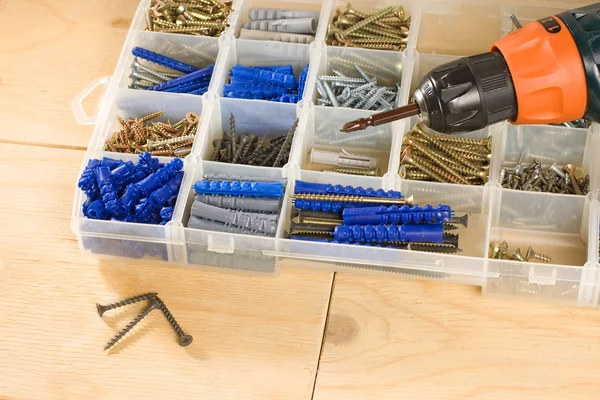 Broca sem fio, parafusos e caixa de ferramentas em um fundo de madeira — Fotografia de Stock