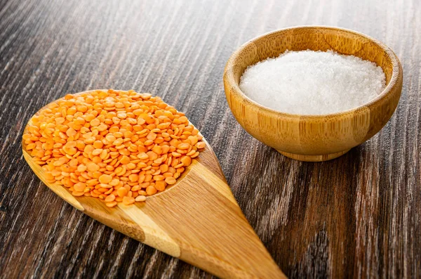 Bamboo spoon with dry red lentils, salt cellar on dark wooden table