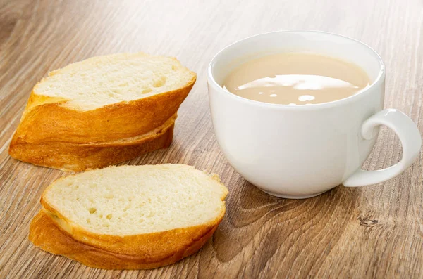 Slices of wheat bread, white glass cup with fermented baked milk on wooden table