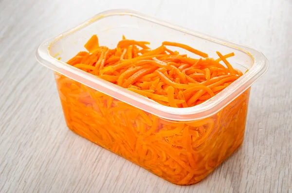 Korean carrot salad in transparent plastic box on wooden table