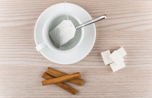 Cup with tea bag, cinnamon sticks and pieces of sugar