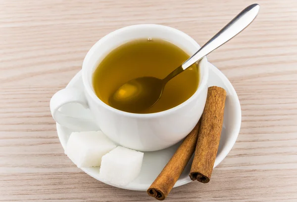 Cup of hot green tea, sugar cubes and cinnamon sticks