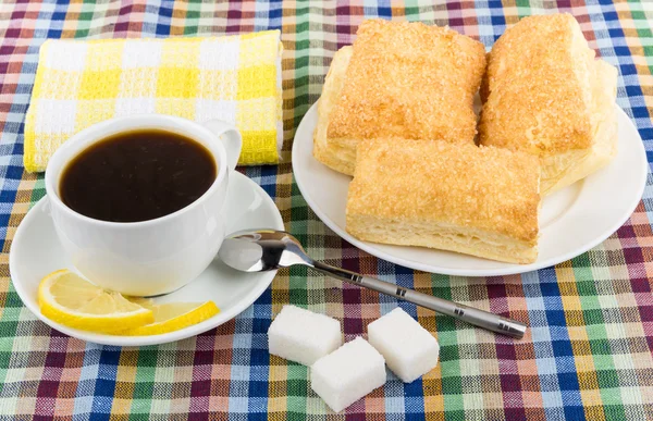 Coffee, lemon and sugar, plate with flaky biscuits on tablecloth