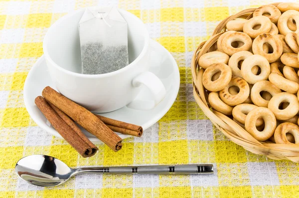 Packet of tea in cup, cinnamon and small bread rings