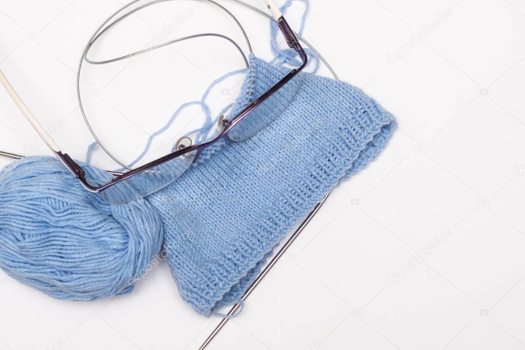 knitting needles and blue ball of thread on white backgroun