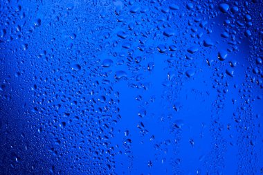 Su damlaları mavi arka plandaki cama düşer.
