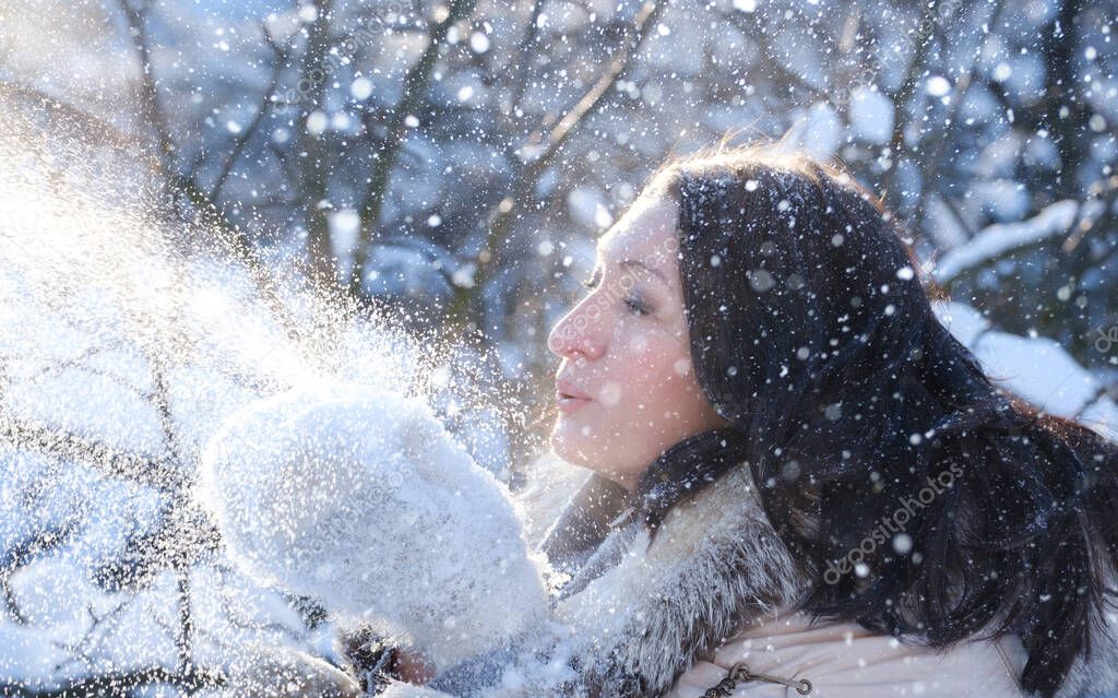 portrait of a woman blowing on the snow in her mittens