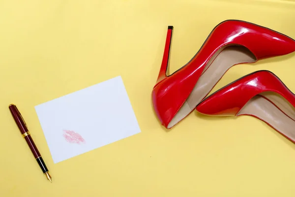 beautiful female shiny red stilettos and a card with a lipstick print  on a yellow background