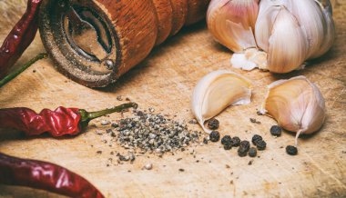 Ahşap kesme tahtasının üzerinde kara biber, kırmızı biber ve sarımsak.