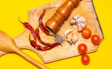 Kara biber, kırmızı biber ve sarımsak. Sarı arka planda tahta kesim tahtasının üzerinde.