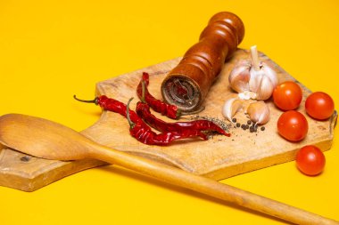 Kara biber, kırmızı biber ve sarımsak. Sarı arka planda tahta kesim tahtasının üzerinde.