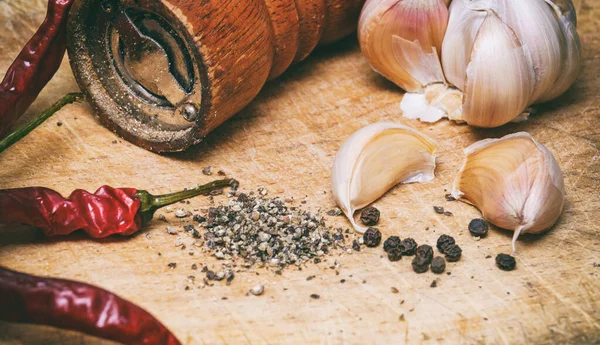 Ahşap kesme tahtasının üzerinde kara biber, kırmızı biber ve sarımsak.