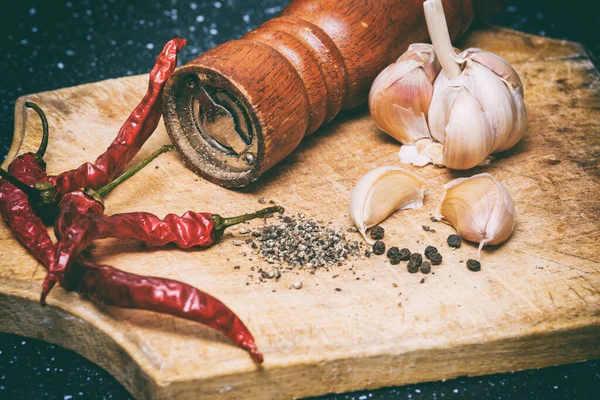 Ahşap kesme tahtasının üzerinde kara biber, kırmızı biber ve sarımsak.