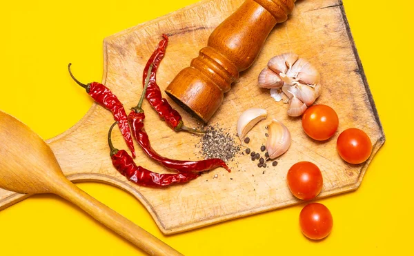 Kara biber, kırmızı biber ve sarımsak. Sarı arka planda tahta kesim tahtasının üzerinde.