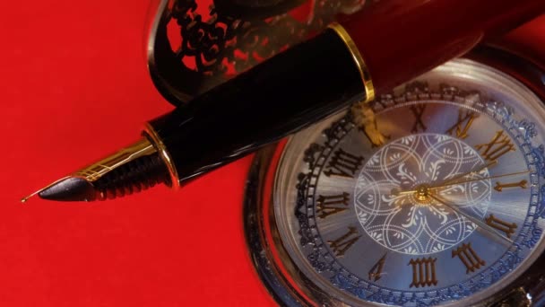 Reloj de bolsillo y pluma estilográfica de cerca sobre un fondo rojo — Vídeos de Stock