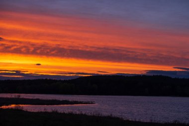 Ufuktaki nehir kıyısının ve ormanın siyah silueti gün batımlı güzel bir gökyüzünün arka planına karşı