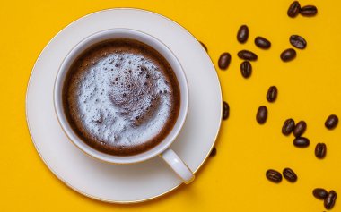 Sarı bir masada bir fincan sade kahve ve tahıl.