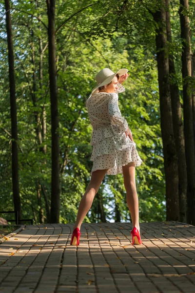 短い夏のドレス 広い帽子と公園で朝のハイヒールの靴で細い女性 — ストック写真