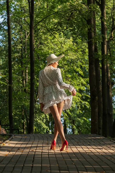 短い夏のドレス 広い帽子 ストッキング 公園で朝のハイヒールの靴を着た女性 — ストック写真