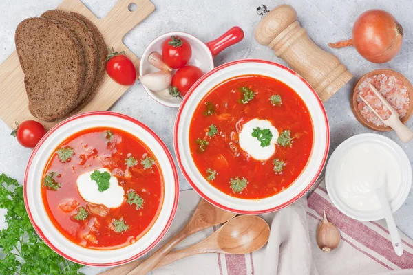 ビートルのトマトスープ赤いボルシチとサワークリーム ライ麦パン パセリとニンニクを2つの白いボウルに入れて灰色のコンクリートの背景 — ストック写真